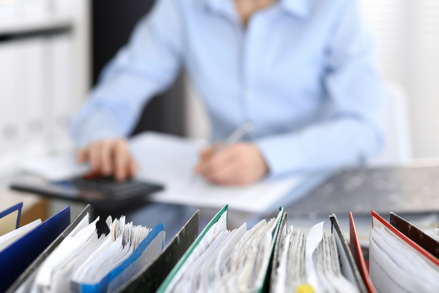 Binders with papers are waiting to be processed with businesswoman or secretary back in blur.