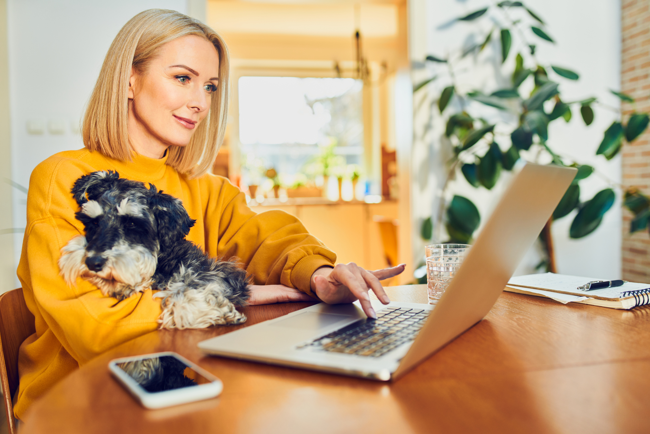 Mid adult woman using laptop at home office sitting with dog at a table