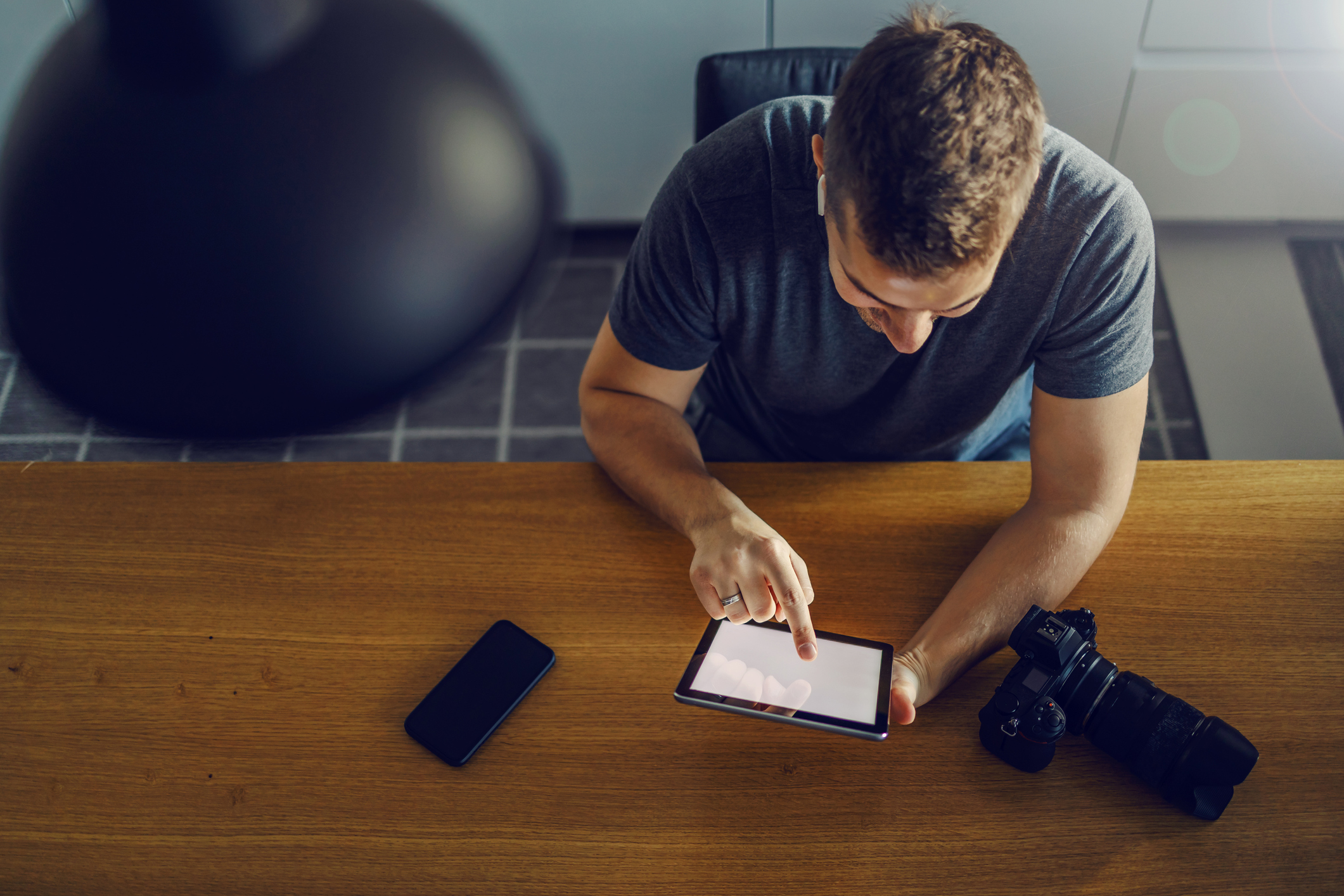 The life of a photographer in one image. A professional man sits behind a kitchen board with a black camera with a smart phone and uses a tablet to organize and plan work. Mockup tablet, freelance job