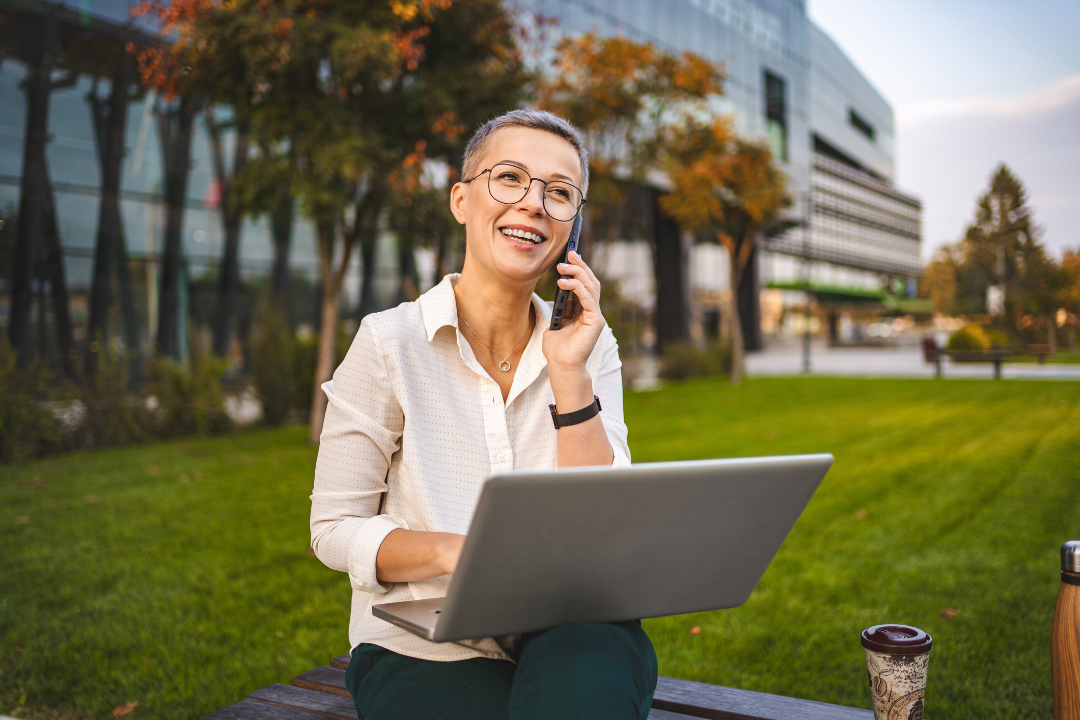 Businesswoman working with laptop and talking on phone in a park